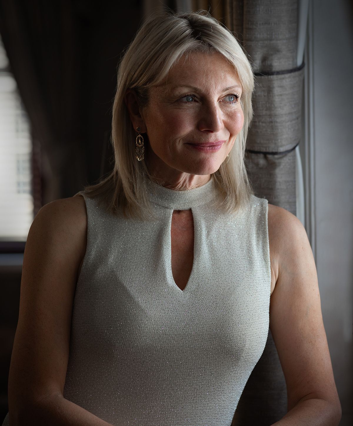 Woman in shimmering dress, softly smiling indoors.