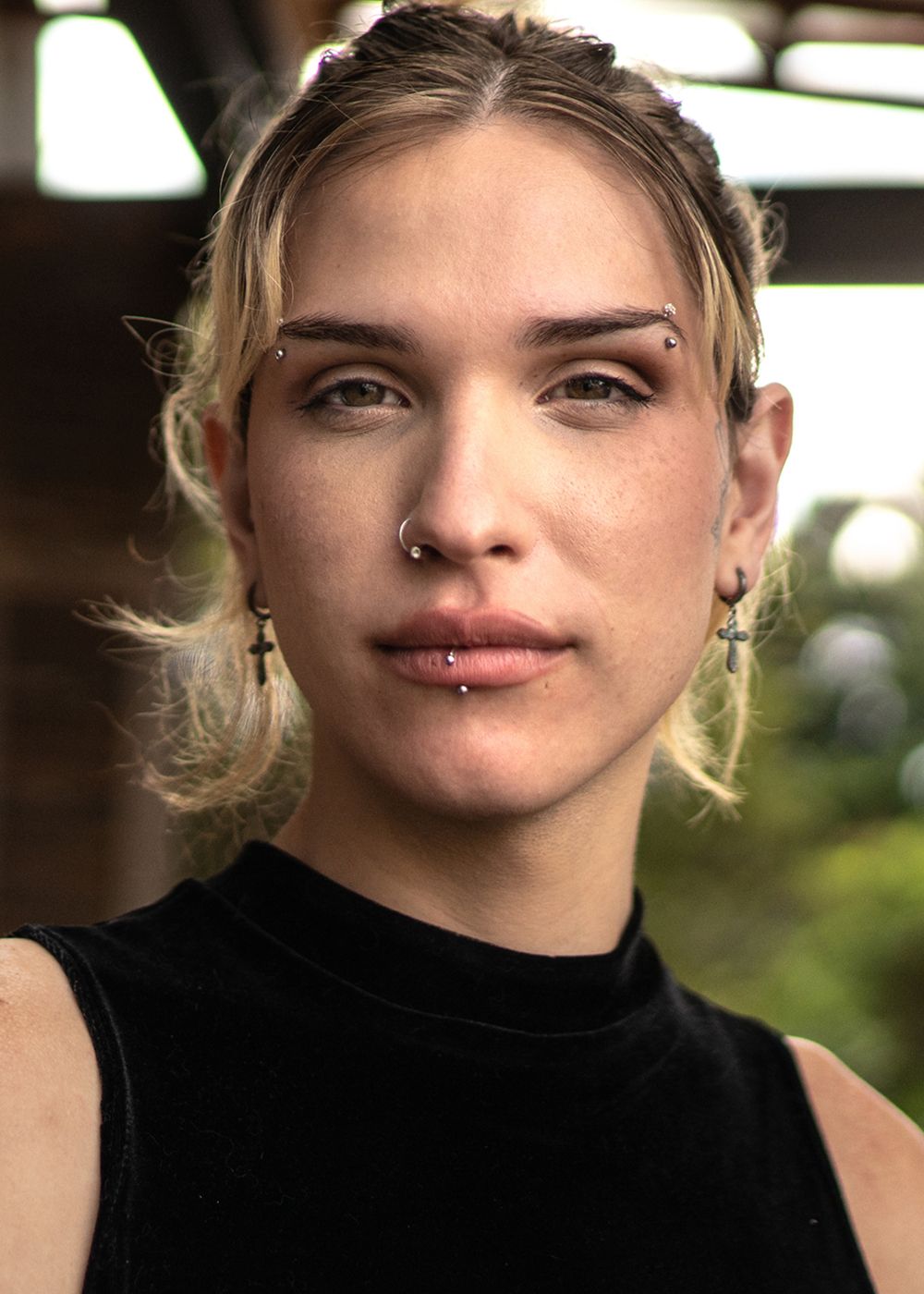 Person with piercings and light hair, serious expression.