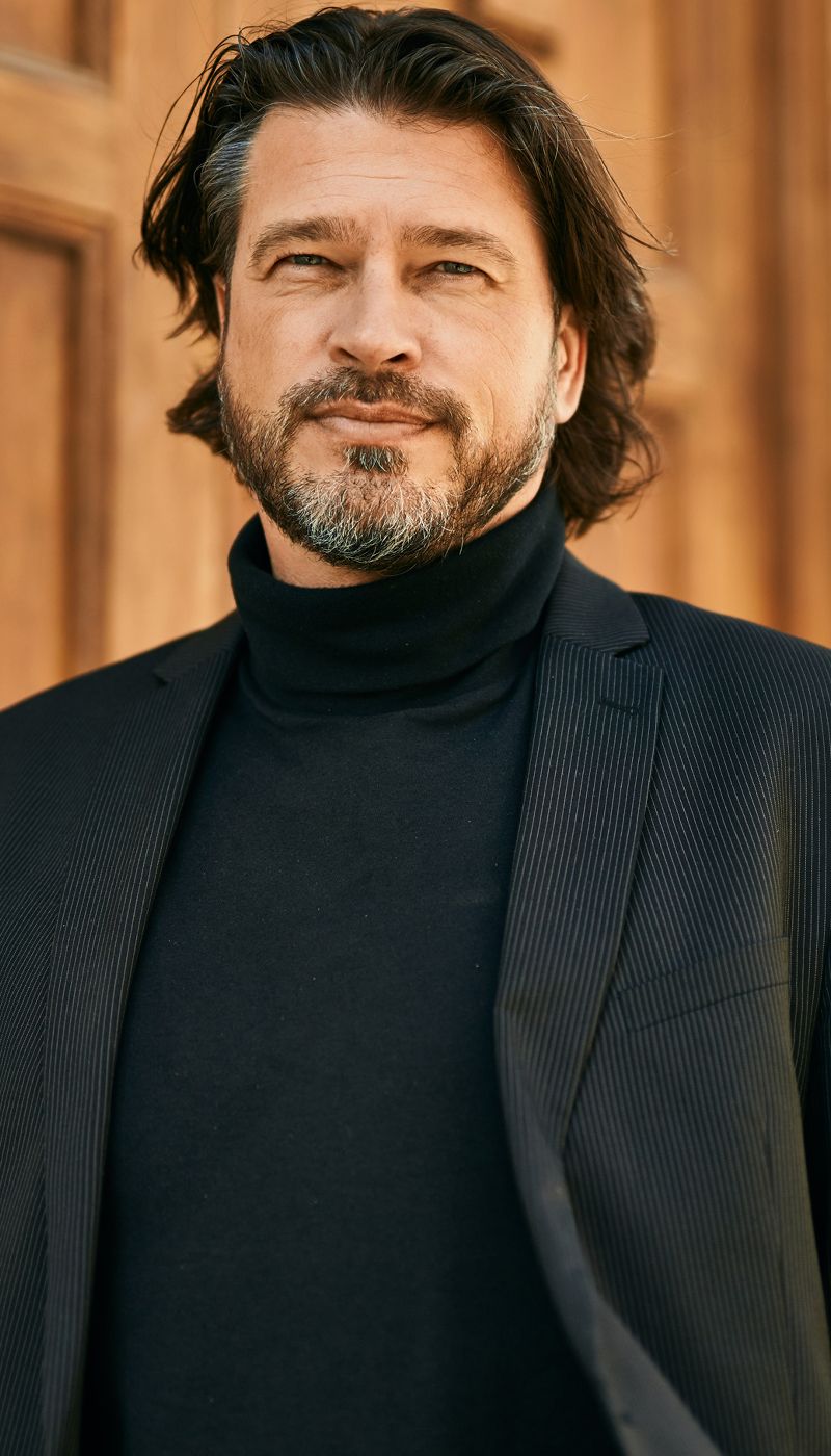 Smiling man in a black turtleneck and blazer.