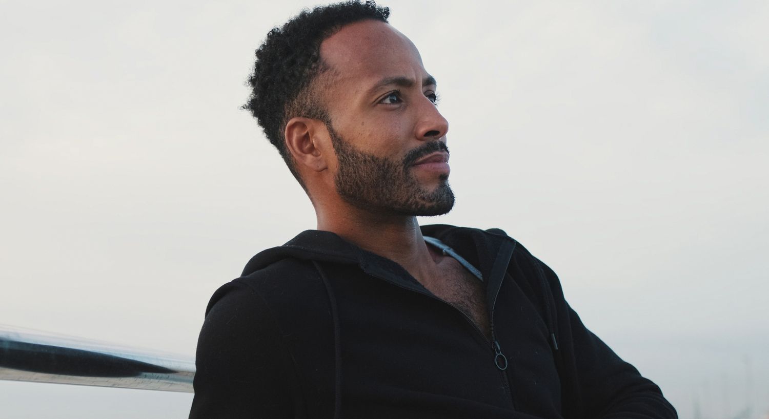 Man in black hoodie looking thoughtfully outdoors.